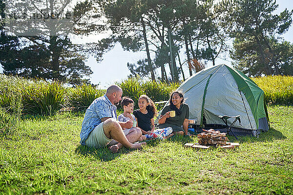 Fröhliche Familie redet und trinkt vor dem Zelt auf einem sonnigen Sommercampingplatz