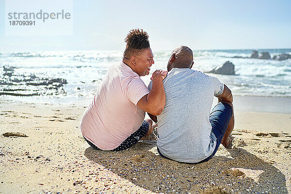 Schwules männliches Paar lacht am sonnigen Meeresstrand