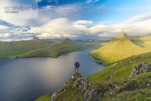 Wanderer mit Rucksack genießt die Aussicht auf Felsen mit Blick auf den Funningur-Fjord  die Insel Eysturoy  die Färöer-Inseln  Dänemark  Europa