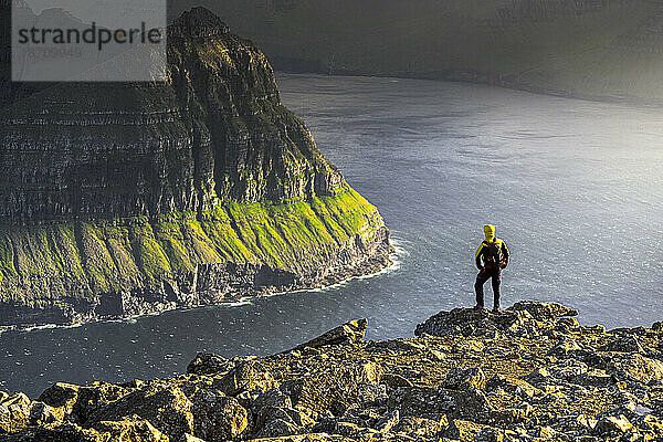 Ein Mann bewundert die majestätischen Klippen entlang eines Fjords  der während einer Wanderung auf der Spitze eines Berges steht  Vidoy Island  Färöer-Inseln  Dänemark  Europa