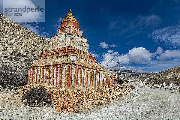 Bunt bemalte buddhistische Stupa vor Berglandschaft  erodierte Landschaft und dahinter Häuser von Garphu  Garphu  Königreich Mustang  Himalaya  Nepal  Asien