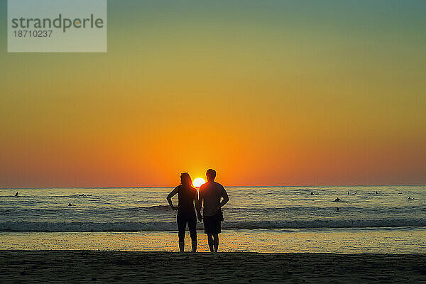 Ein Paar hält Händchen am Strand von Guiones  wo sich Menschen zum Surfen und Beobachten des Sonnenuntergangs versammeln  Playa Guiones  Nosara  Guanacaste  Costa Rica  Mittelamerika