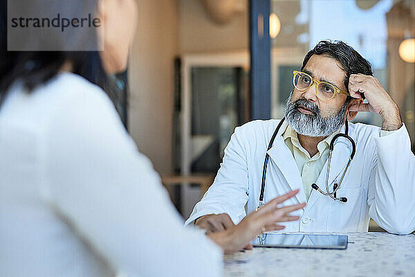 Reife Ärztin hört einer Patientin zu  die in der Klinik sitzt