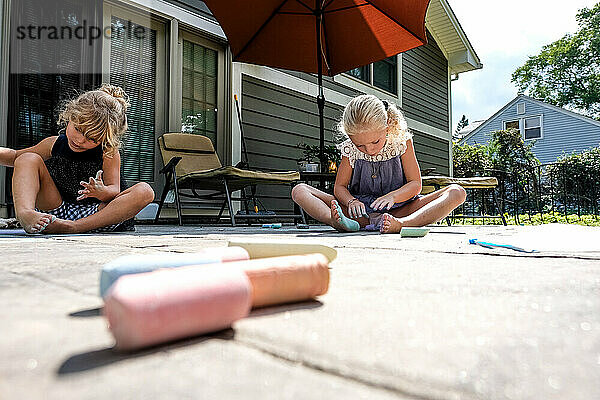 Zwei Mädchen spielen draußen im Sonnenlicht auf der Terrasse mit Kreide