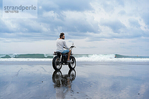 Stilvoller Mann reist auf einem Motorrad am Meeresstrand.