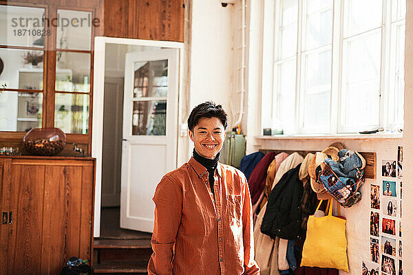 Fröhliche asiatische Person  die im lichtdurchfluteten Zuhause mit Mänteln lächelt