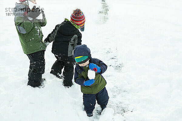 Drei Brüder spielen nach einem Wintersturm draußen und machen Schneebälle