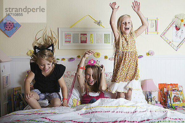 Drei junge Mädchen springen aufs Bett.