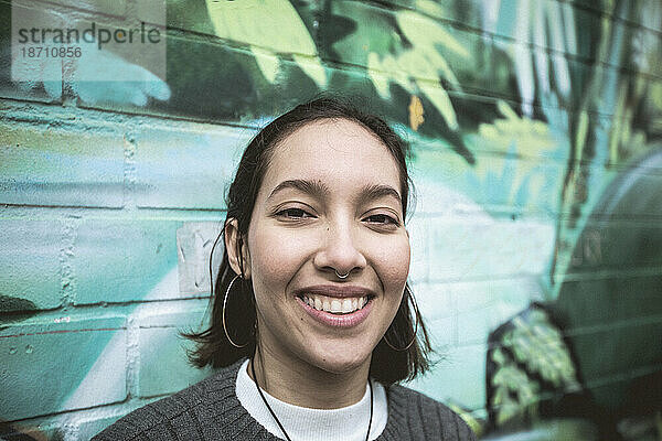 Junge Frau mit offenem Lächeln steht neben einer farbenfrohen Graffitiwand