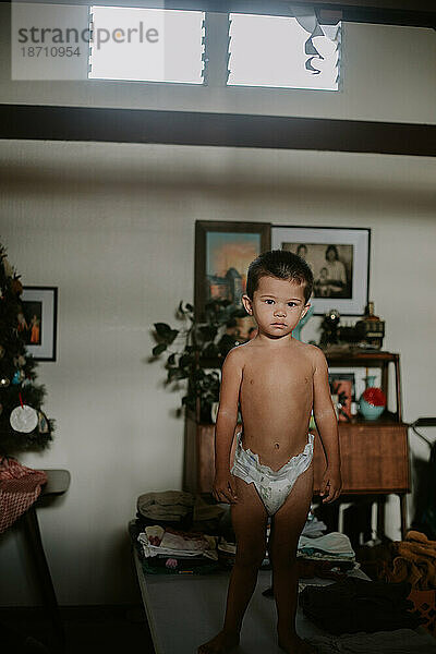 Multiracial Asian toddler boy standing on a table in his diaper