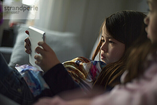 Junges asiatisches Mädchen auf dem Sofa  das zu Hause mit ihrem Tablet spielt