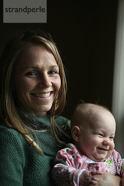 Eine Mutter hält ihr Baby und lächelt vor schwarzem Hintergrund.