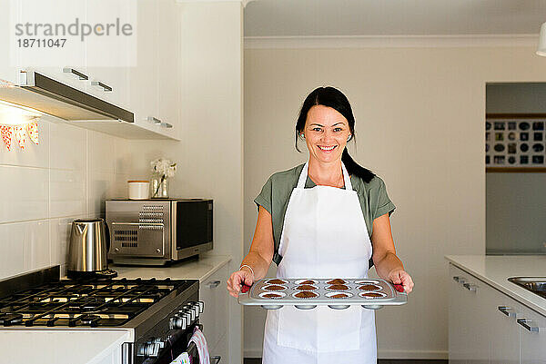 Unternehmerbäcker hält ein Tablett mit Cupcakes neben dem Ofen