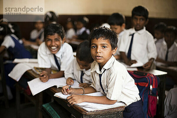 Ein kleiner Schuljunge blickt von seinem Schreibtisch in einer kleinen Schule auf.