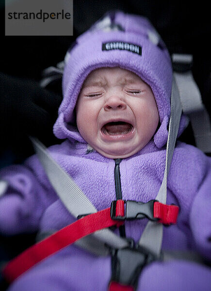 Ein für den Winter eingepacktes Baby weint in seinem Kinderwagen.