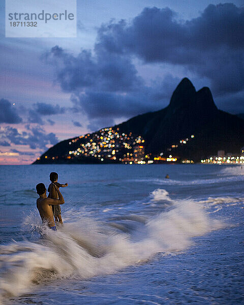 Ein Mann und ein Kind spielen in den Wellen am Strand von Ipanema  während die Sonne untergeht  Rio de Janeiro  Brasilien.