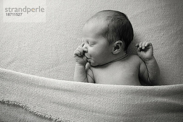 Baby lutscht Daumen auf einer Decke in Schwarz und Weiß