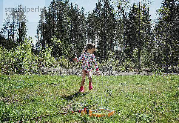 Junges Mädchen läuft spielend durch eine Sprinkleranlage in ihrem Garten