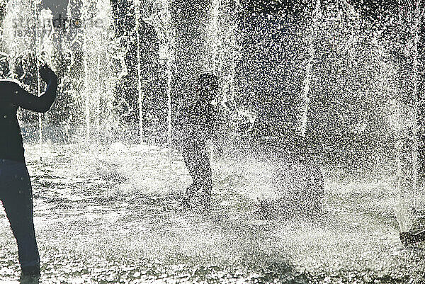 Silhouette von Kindern  die sich während der Hitzewelle in einem Brunnen abkühlen