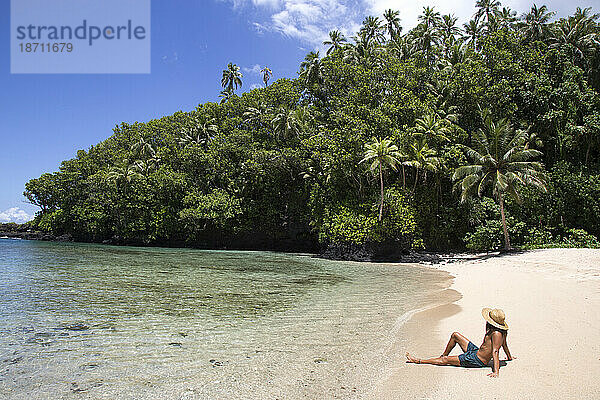 Ein fitter Mann mit Hut bräunt sich am abgelegenen tropischen Strand von Samoa