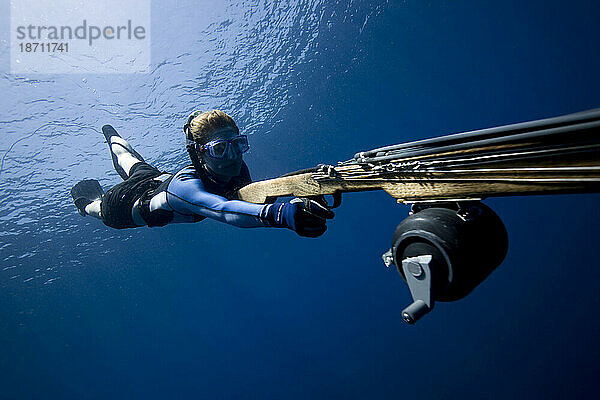 Unterwasseransicht einer Frau  die mit einer Harpune im blauen Wasser Costa Ricas in Richtung Kamera taucht.
