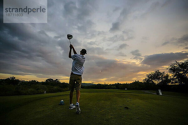 Rückansicht eines Mannes  der bei Sonnenuntergang Golf spielt