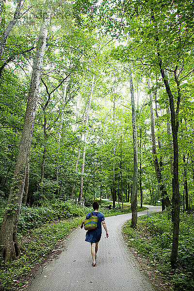 Eine junge Frau geht einen Weg unter grünen Bäumen entlang.