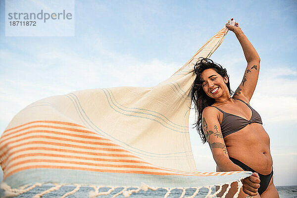 Latina-Frau vergnügt sich am Strand mit Handtuch im Wind
