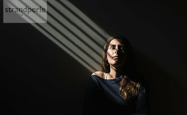 Porträt einer Frau  die mit geschlossenen Augen in einem Lichtfleck sitzt.