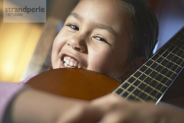 Kleines asiatisches Mädchen hält ihre Akustikgitarre in der Hand und lächelt in die Kamera