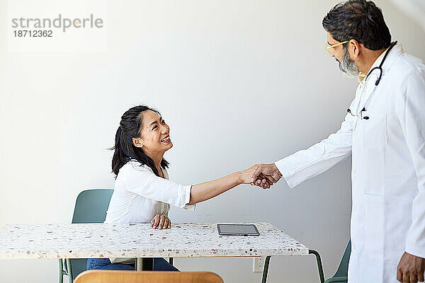 Reifer männlicher Arzt beim Händeschütteln mit Patientin in der Klinik