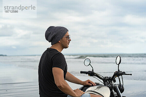 Junger Mann fährt mit einem Retro-Motorrad am Strand.