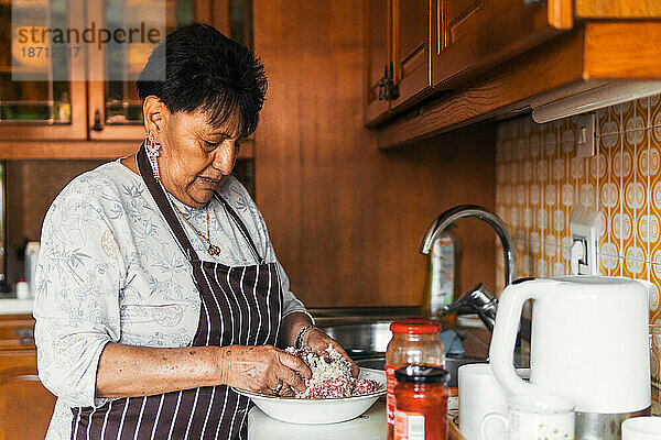 Ältere lateinamerikanische Frau knetet Fleisch und kocht in der Küche
