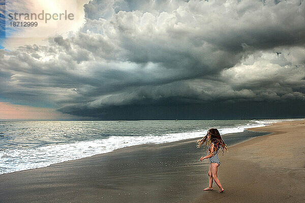 Junges Mädchen am Strand unter stürmischem Himmel