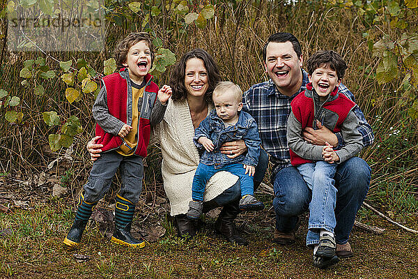 Eine lachende  glückliche Familie sitzt eng aneinandergereiht in einer grasbewachsenen Prärie