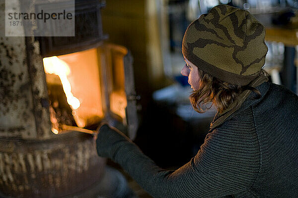 Eine Frau heizt einen sehr alten Dickbauchofen in einer rustikalen Hütte in Telluride  Colorado. Ihr Gesicht wird von den Flammen des Feuers beleuchtet.