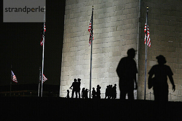 Silhouetten von Menschen  die an den leistungsstarken Lichtern vorbeigehen  die nachts auf dem Washington Monument in Washington  D.C. leuchten.