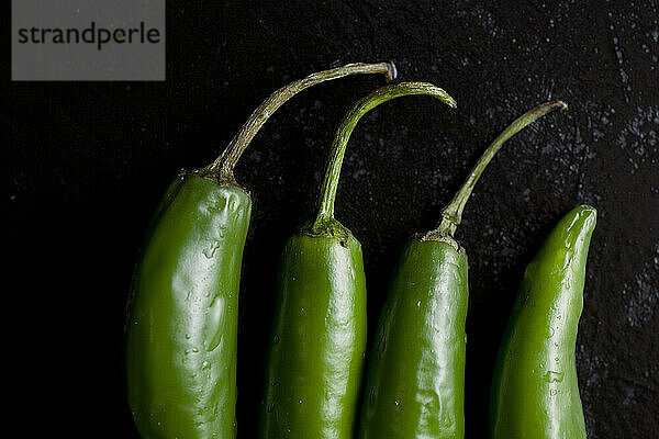 Mehrere scharfe grüne Bio-Paprika liegen auf einem nassen schwarzen Schneidebrett in einer heimischen Küche in Seattle  Washington.