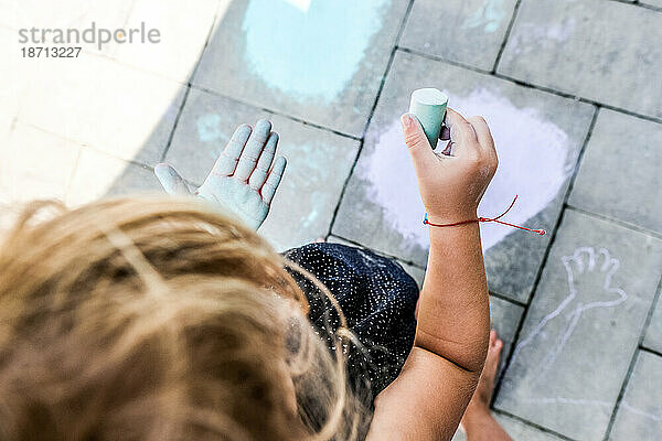 Kleines Mädchen spielt draußen auf der Terrasse mit Kreide und färbt die Hand in der Sonne