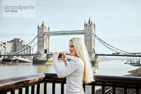Attraktive nachdenkliche Frau  die ein Foto von der Tower Bridge macht