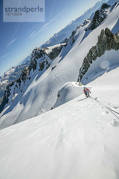 Ein Alpinist macht eine Pause  während er in Frankreich einen langen  steilen Schneeaufstieg in Angriff nimmt