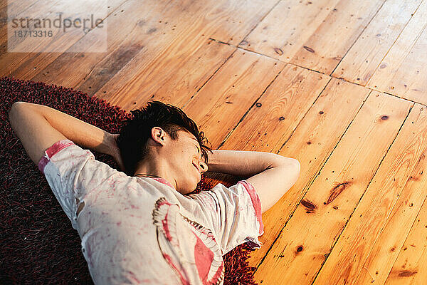 Asiatische Person lächelt und streckt sich zu Hause auf dem Teppich auf dem Boden