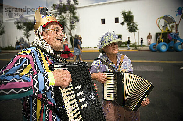 Zwei ältere Männer und Akkordeons bei einer Parade in Santa Barbara. Die Parade umfasst extravagante Festwagen und Kostüme.