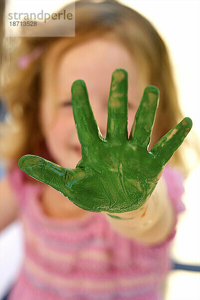 Ein kleines blondes Mädchen hält ihre grün bemalte Hand in die Kamera.