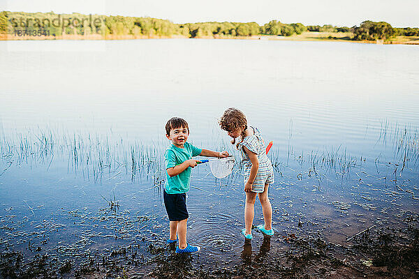 Kleiner Junge zeigt Mädchen einen Fisch  den er im Wasser am See gefangen hat