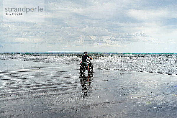 Junger Mann fährt mit einem Retro-Motorrad am Strand.