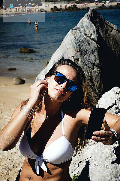 Blonde Frau mit Sonnenbrille nutzt kabelloses Headset und Mobiltelefon.