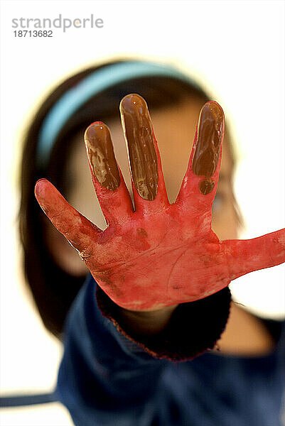 Ein kleines Mädchen hält ihre rot bemalte Hand in die Kamera.
