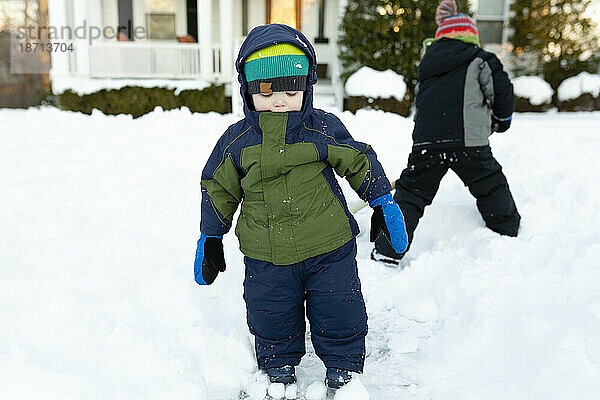 Zwei Jungen stehen im Winter in Winterkleidung im Schnee vor dem Vorgarten