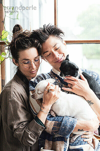 Queeres Paar lächelt und hält seine beiden kleinen Hunde zu Hause zusammen